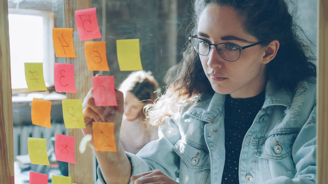 Profissional organizando notas adesivas numeradas em um painel de vidro.