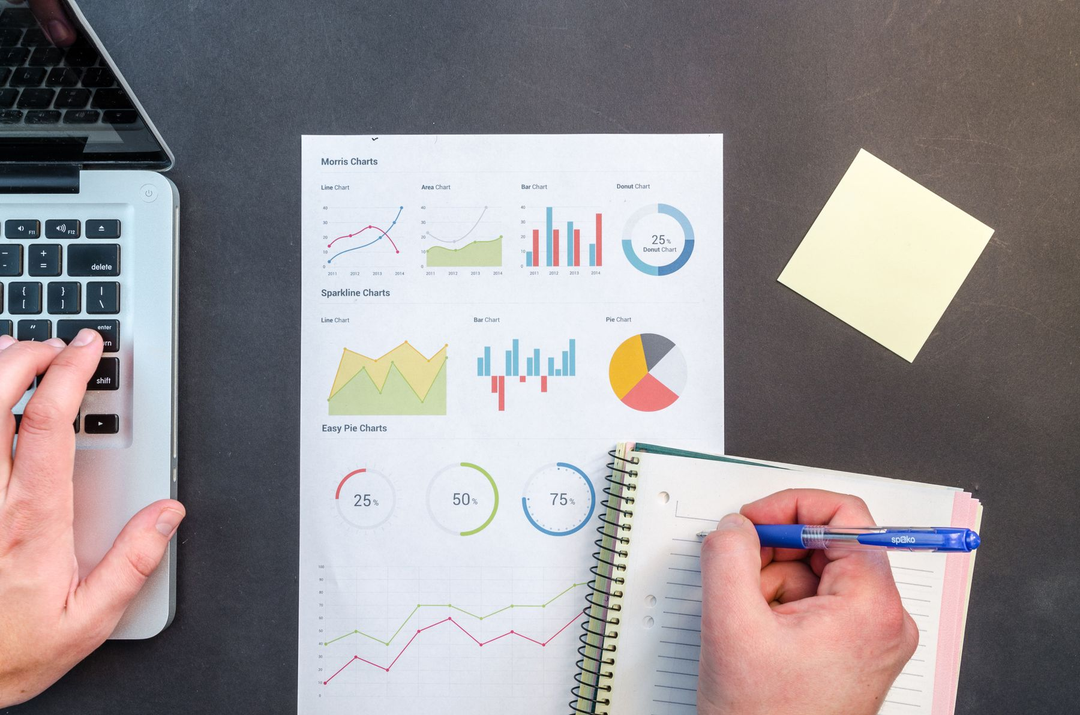 Notebook, documentos e gráficos em uma mesa de trabalho.