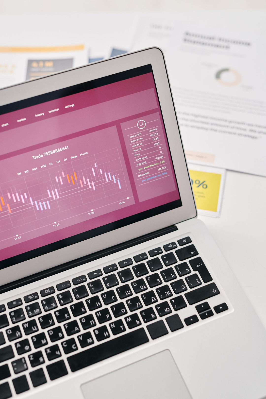 Notebook exibindo um painel com gráficos e indicadores, cercado por relatórios impressos.