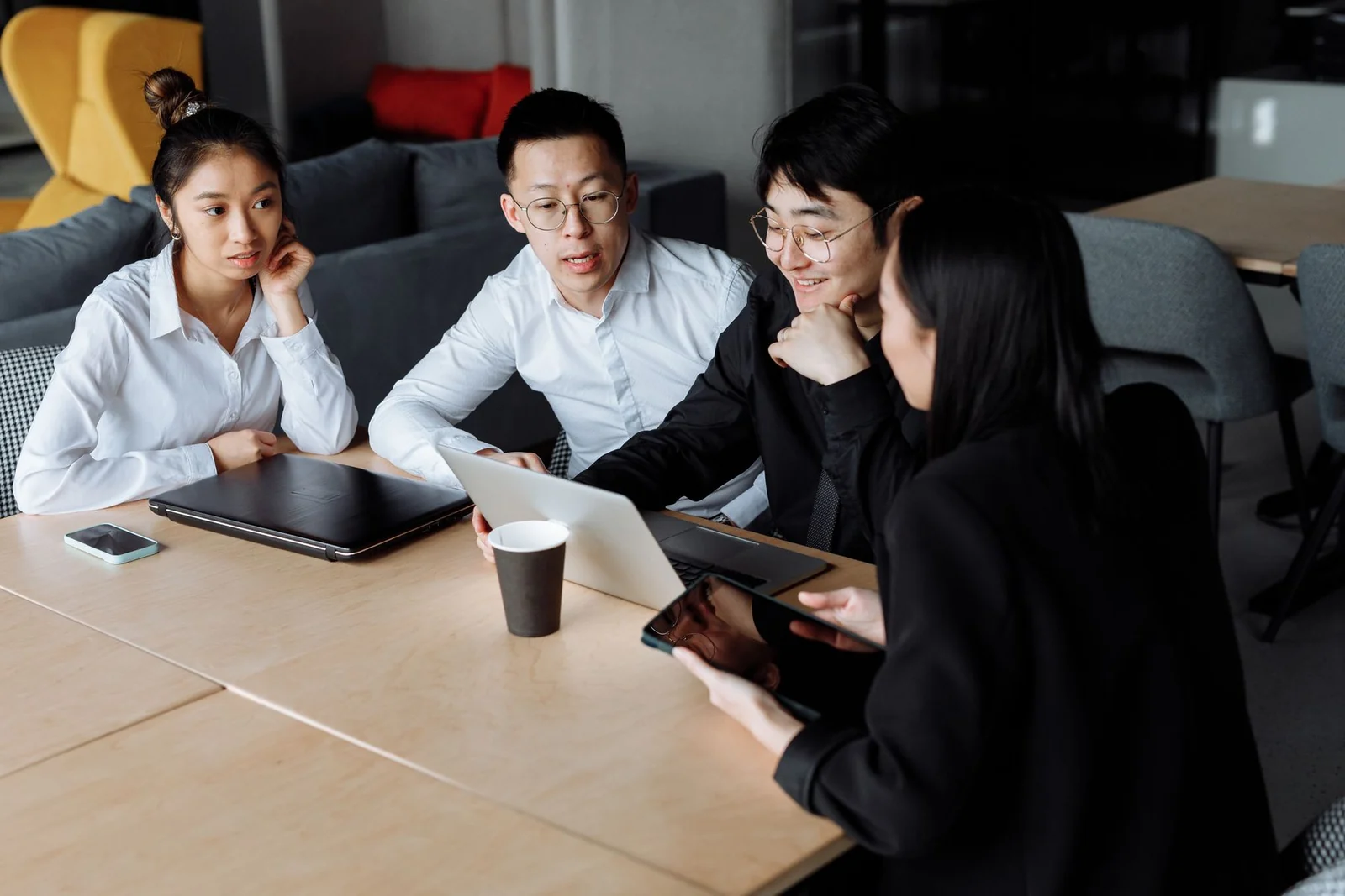 Profissionais reunidos à mesa analisando informações em um notebook.