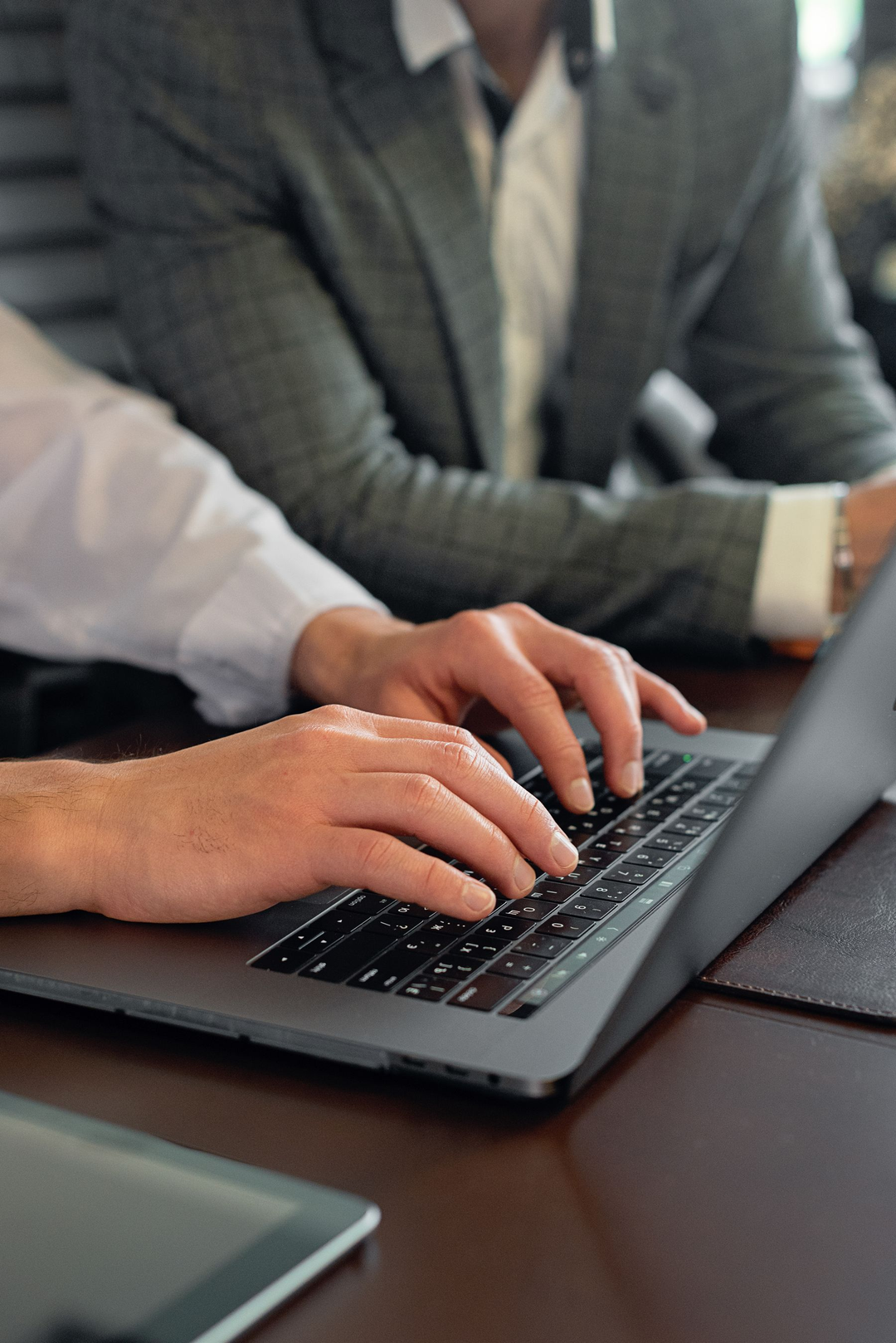 Mãos de um profissional digitando em um notebook durante o trabalho em equipe.
